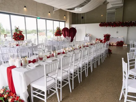The Pavilion set for a reception with long tables, white chairs, red roses and a heart backdrop at The Orchard Penrith