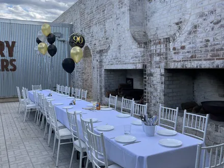 Long table set for a 90th birthday beside the outdoor fireplaces at The Orchard Penrith